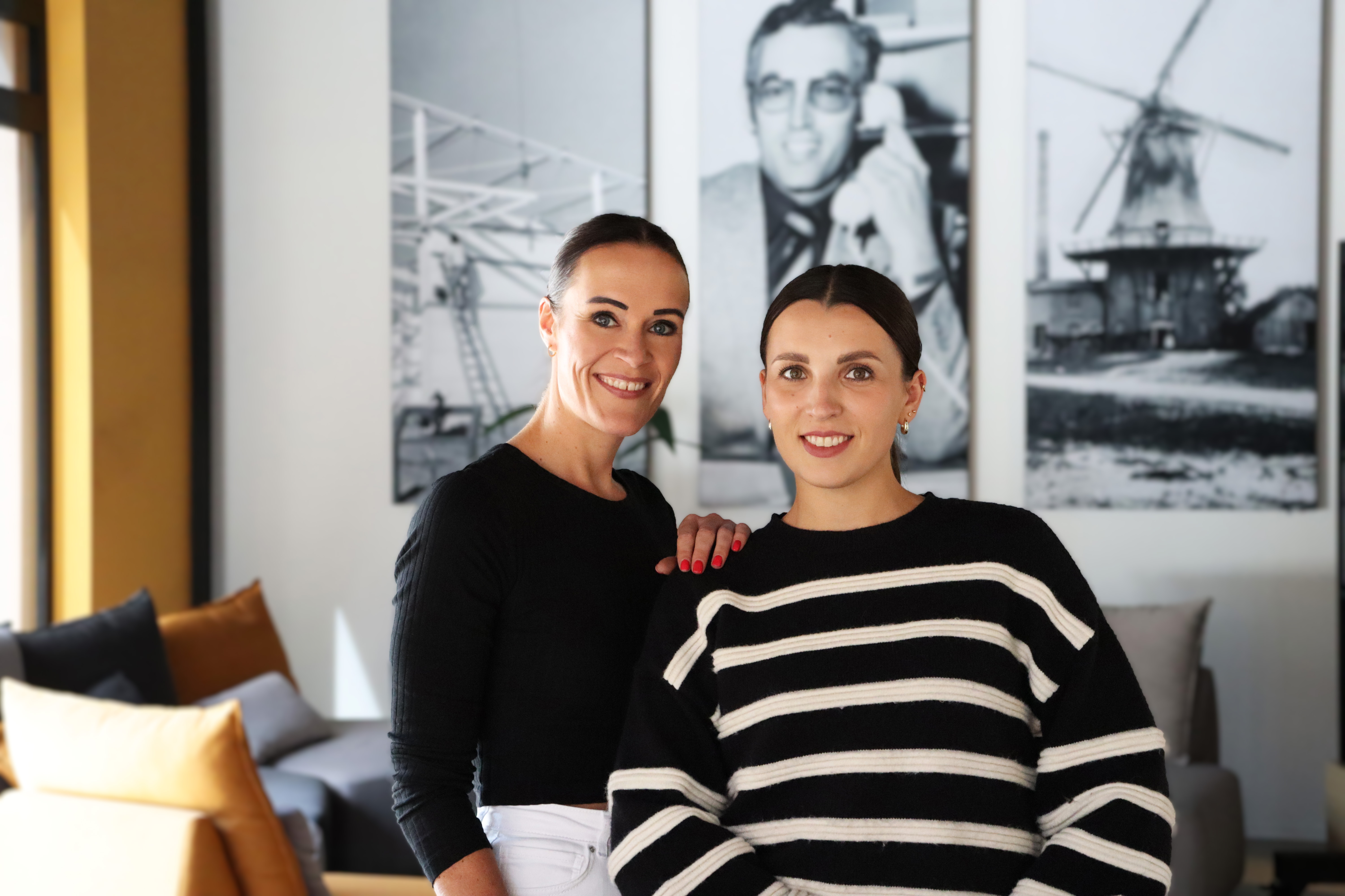 Zwei Mitarbeiterinnen von LOBO HOME stehen in einem modernen Bürobereich mit historischen Bildern im Hintergrund