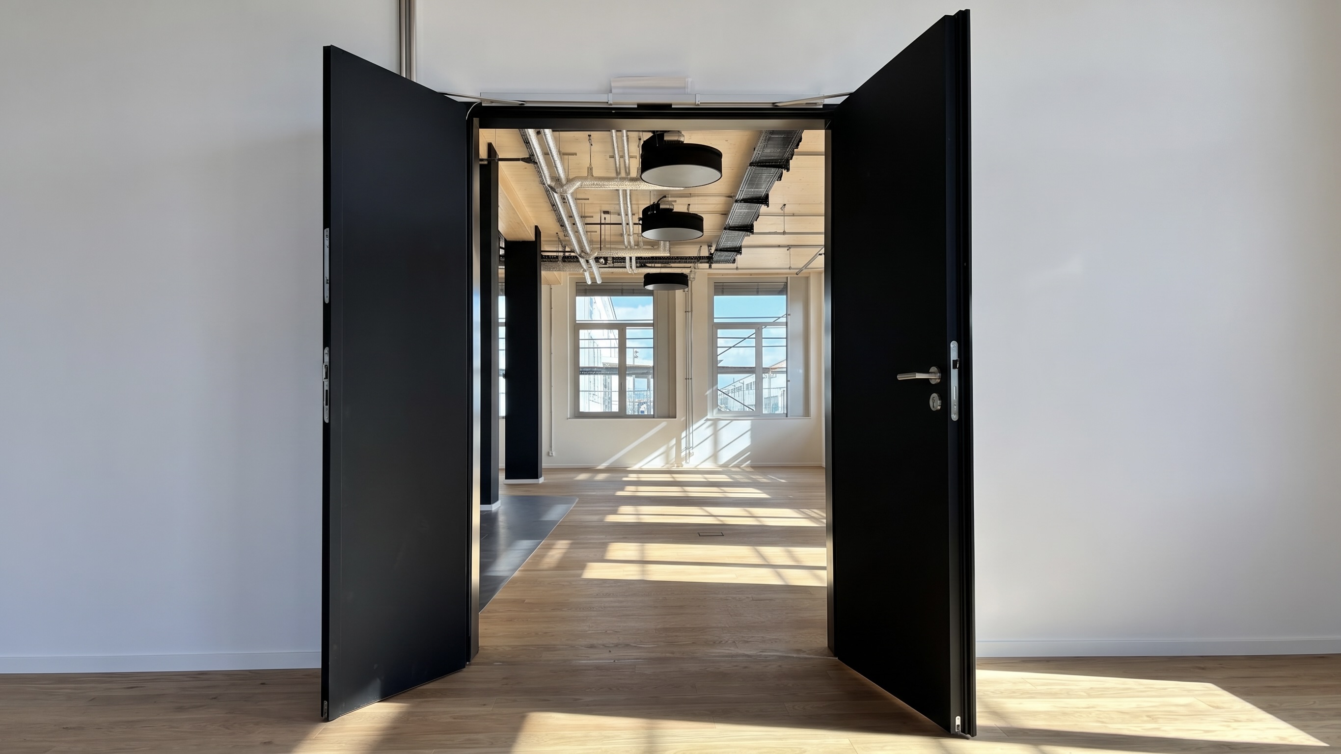 Geöffnete schwarze Sicherheitstür im Lighthouse Bremen mit Blick auf eine helle Bürofläche und Holzoptik-Boden