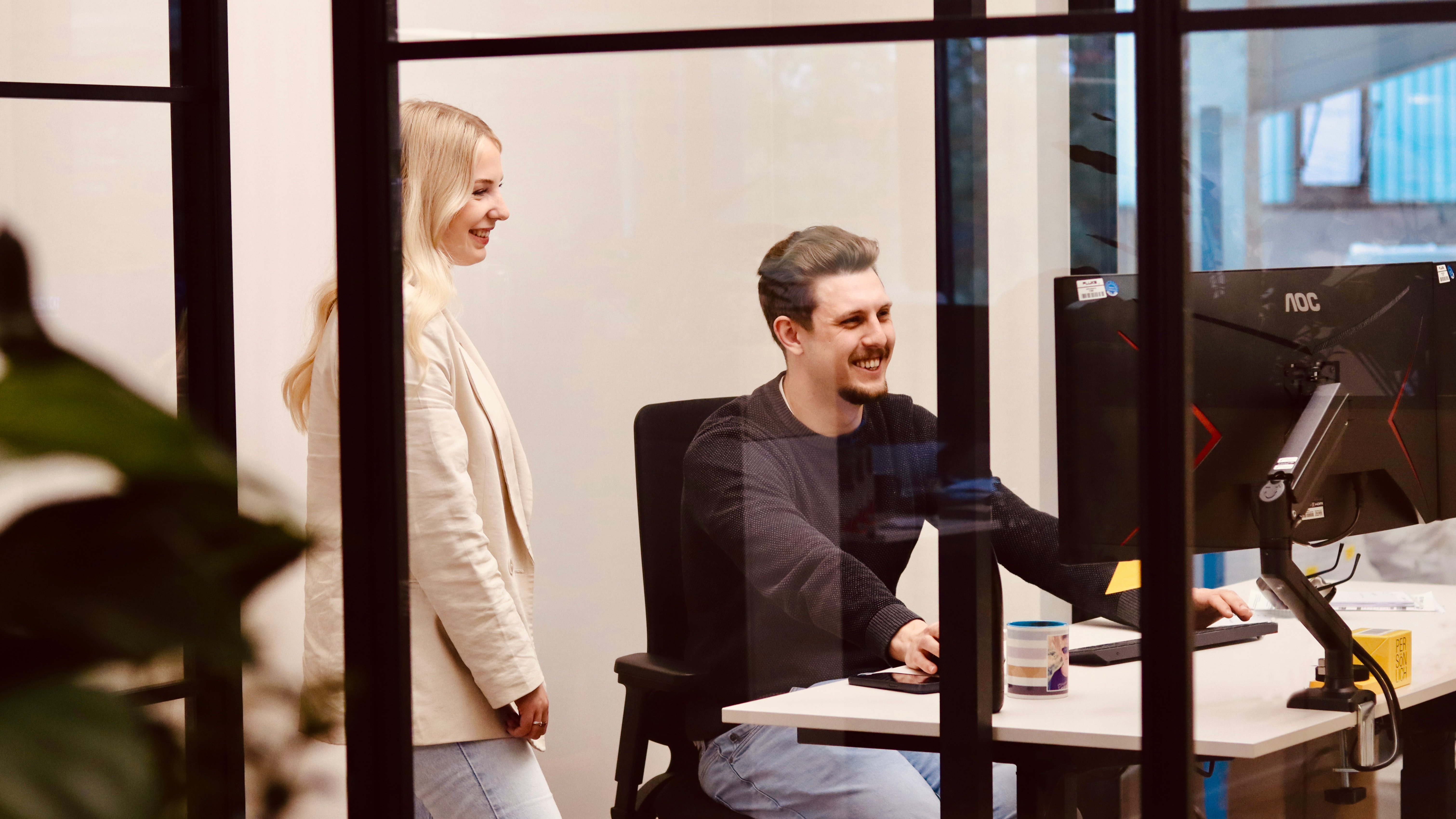 Zwei Personen im LOBO HOME Büro arbeiten gemeinsam an einem Bildschirm hinter einer Glas-Trennwand